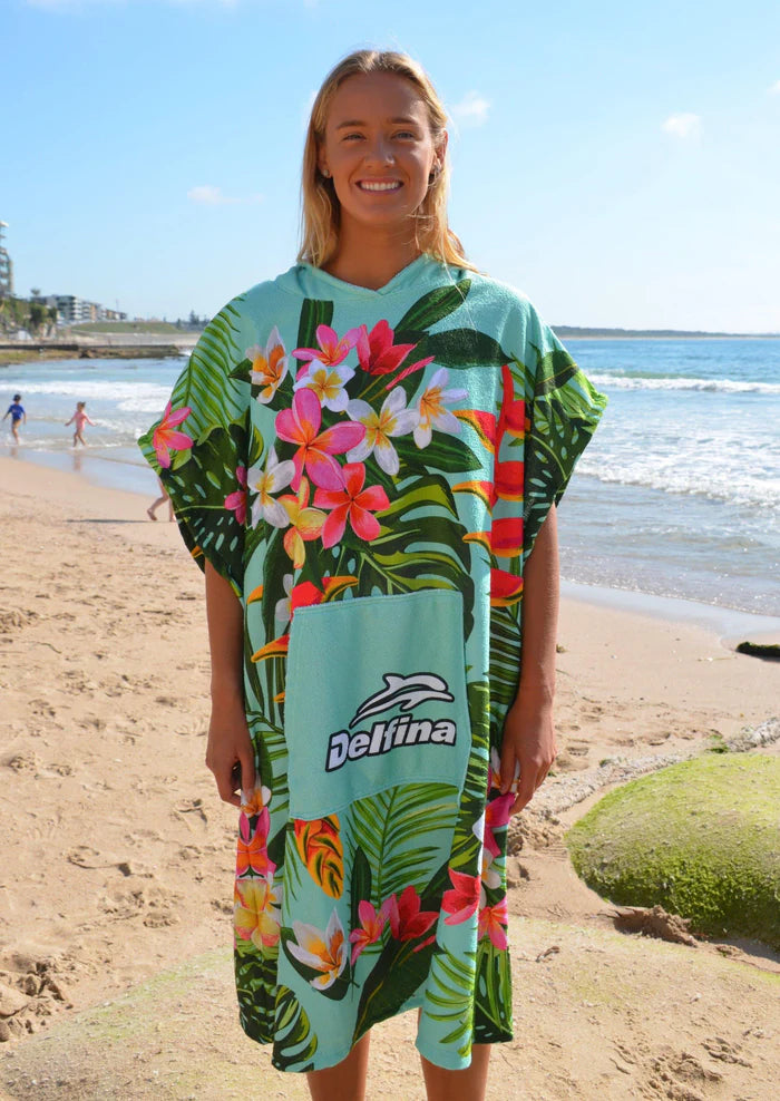 Person wearing a colorful tropical patterned poncho on a beach with ocean and sky in the background